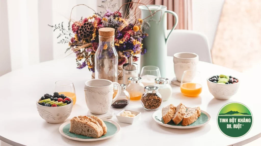 Bàn ăn sáng với bánh mì, trái cây tươi và ngũ cốc dưới ánh sáng tự nhiên, gợi ý bữa ăn dinh dưỡng cân bằng.