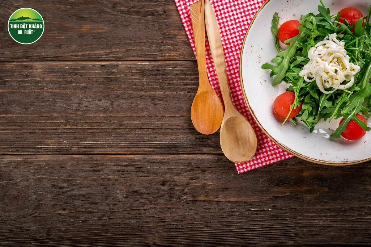 Salad rau arugula, cà chua bi và phô mai tươi trên đĩa trắng, cạnh muỗng gỗ và khăn caro đỏ